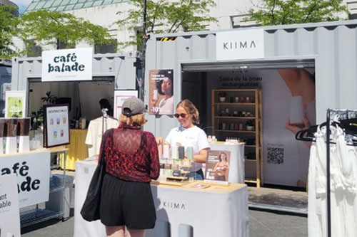 Outdoor market with a Kiima booth set up in a container, where refillable personal care products are displayed on tables.